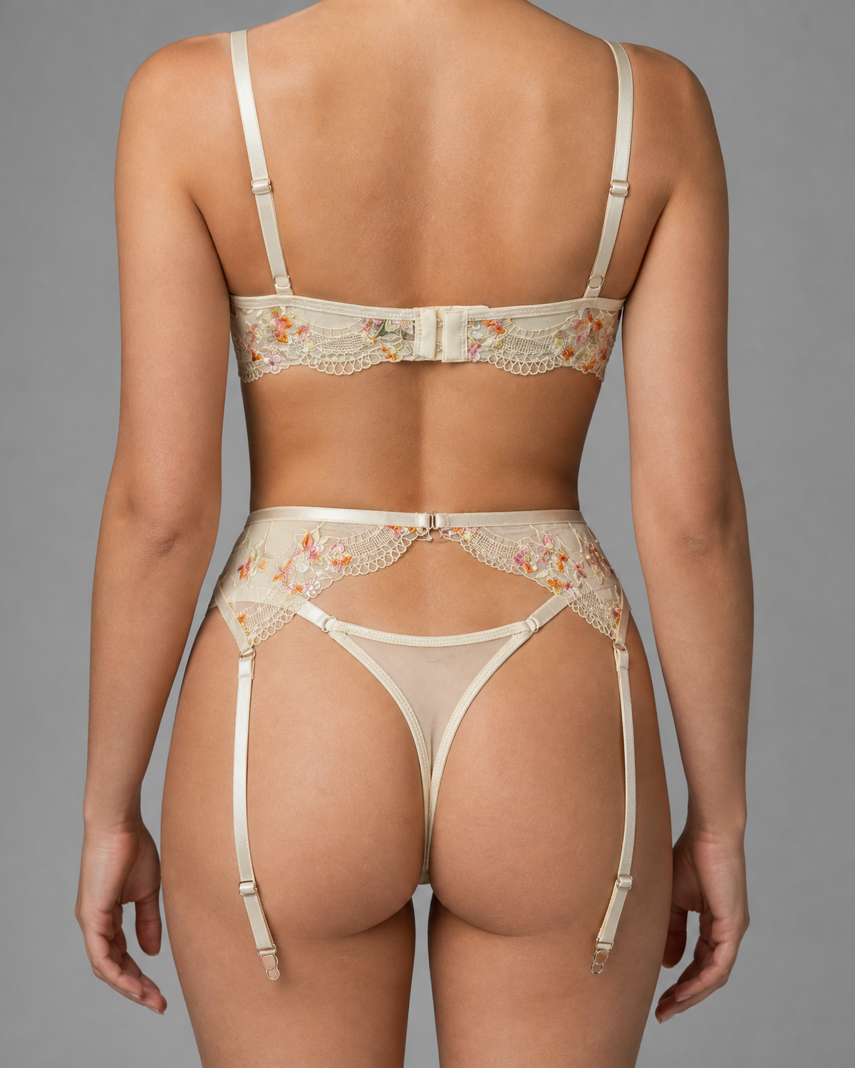 Back view of cream three-piece lingerie set with embroidered mesh bra, high-waisted suspender belt and matching G-string